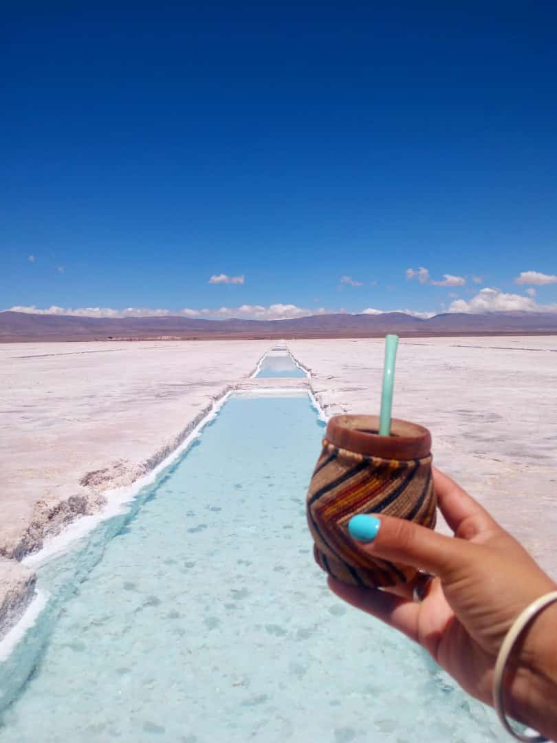 Turista sosteniendo un mate con un piletón en Salinas Grandes, Jujuy